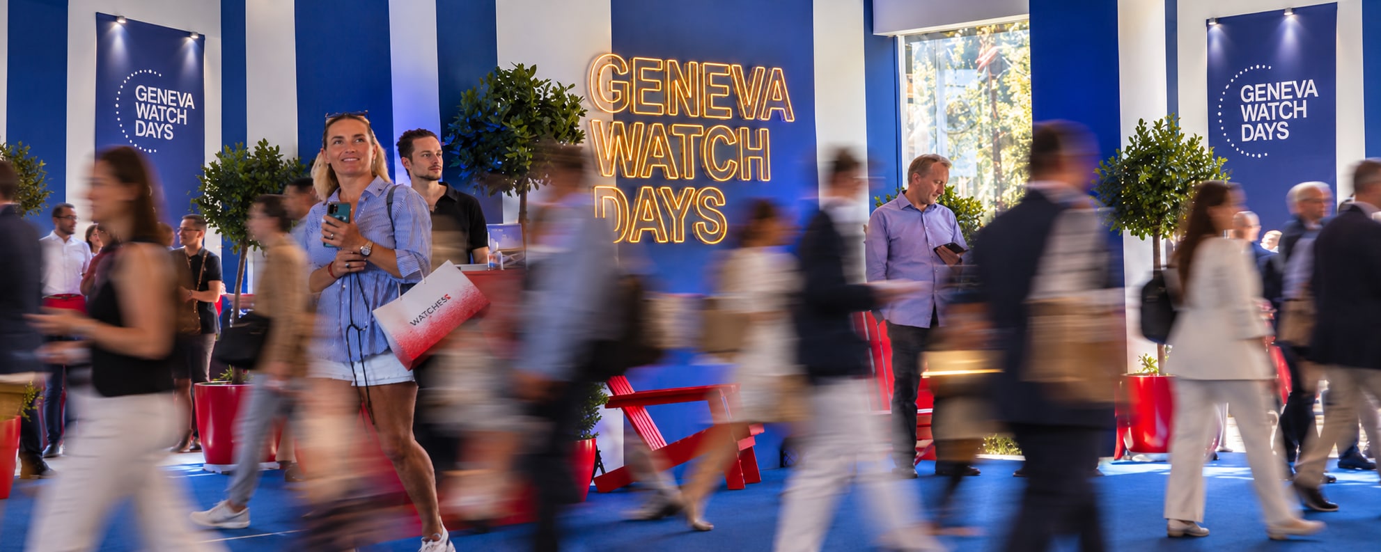 Visitors pass the illuminated Geneva Watch Days sign in Geneva, blurred in motion.
